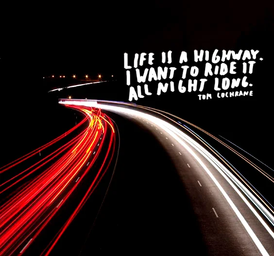 Night Ride Captions For Instagram: Long-exposure night photograph of a winding highway showing red and white light trails left by moving vehicles against a black background. On the top-right side, white stylized handwritten text quotes Tom Cochrane: "LIFE IS A HIGHWAY. I WANT TO RIDE IT ALL NIGHT LONG."